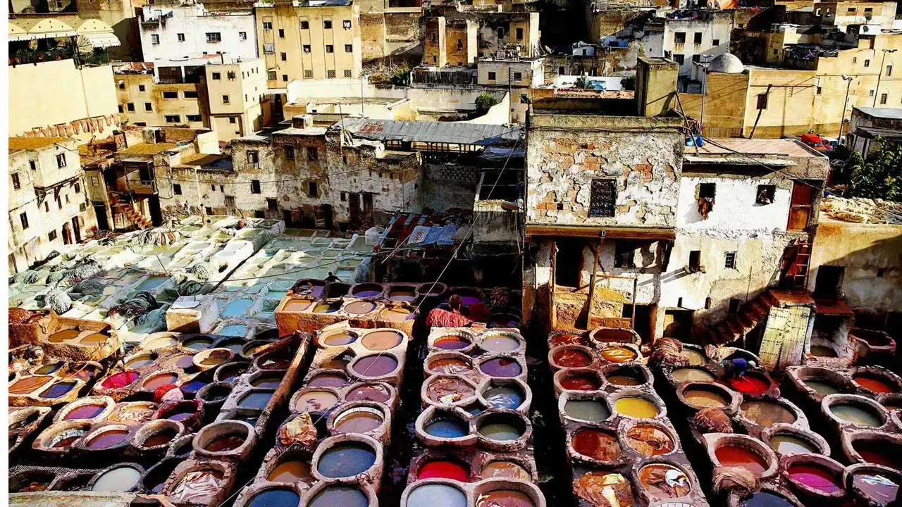 Panoramic view of the Fes Tanneries, highlighting the traditional leather-making process with colorful dye-filled stone vats and the bustling atmosphere of the medina.